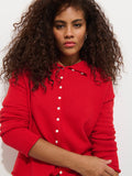 A woman with long, curly brown hair wears the Taylor Cardigan in cotton cashmere, featuring hand-finished details, and faces the camera against a plain white background.