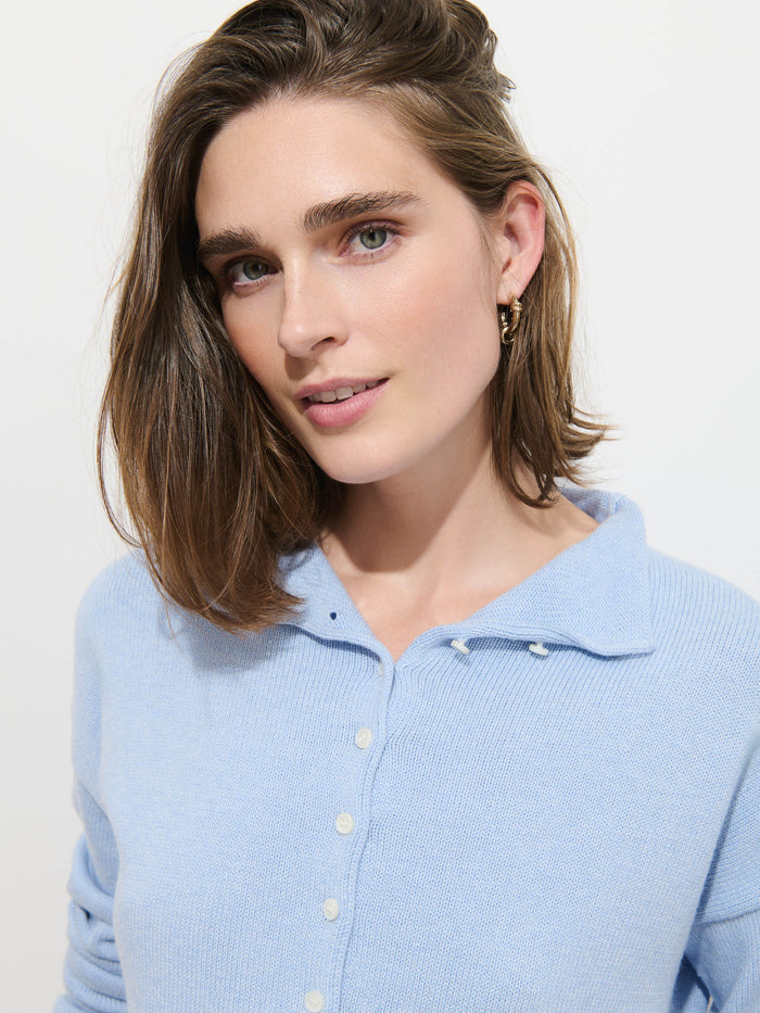 A woman with light brown hair wearing the Taylor Cardigan in Cotton Cashmere, featuring Troca shell buttons, stands against a plain white background and looks at the camera.