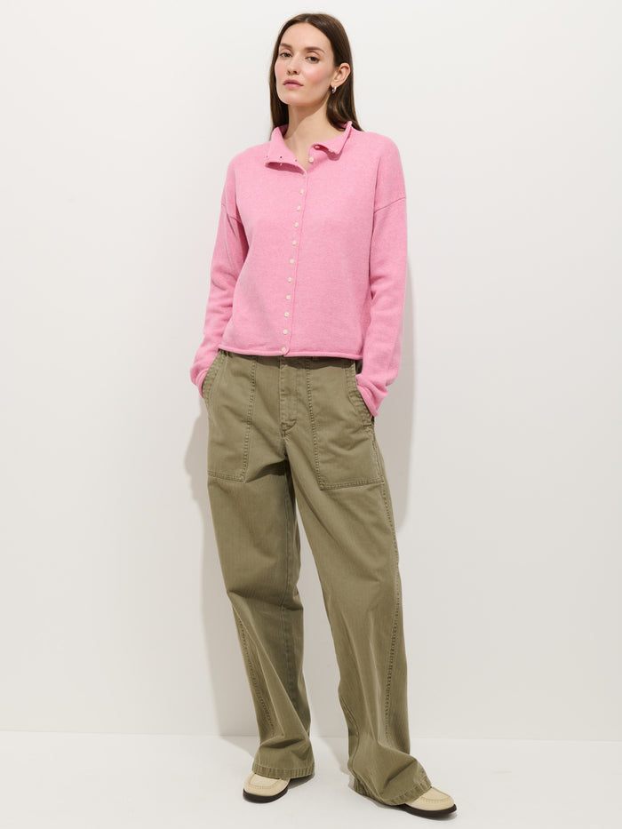 Against a white background, a person wears the Taylor Cardigan in Cotton Cashmere—light pink and oversized—paired with loose olive cargo pants and beige sneakers, hands in pockets and expression neutral.