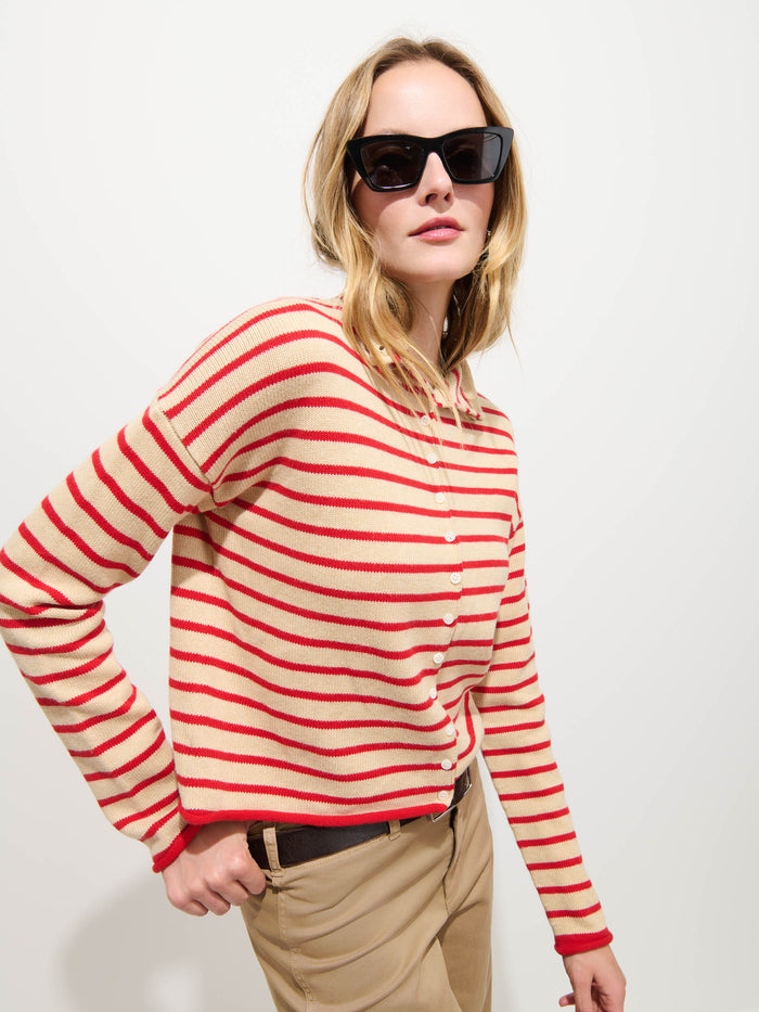 A woman in black sunglasses wears the Taylor Striped Cardigan in Cotton Cashmere—an oversized red-and-white striped sweater—paired with beige pants, standing against a plain white background.