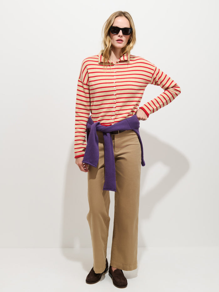 Woman in sunglasses wearing the Taylor Striped Cardigan in Cotton Cashmere, styled with khaki wide-leg pants, brown shoes, and a purple luxury knitwear sweater tied around her waist, standing against a plain white background.
