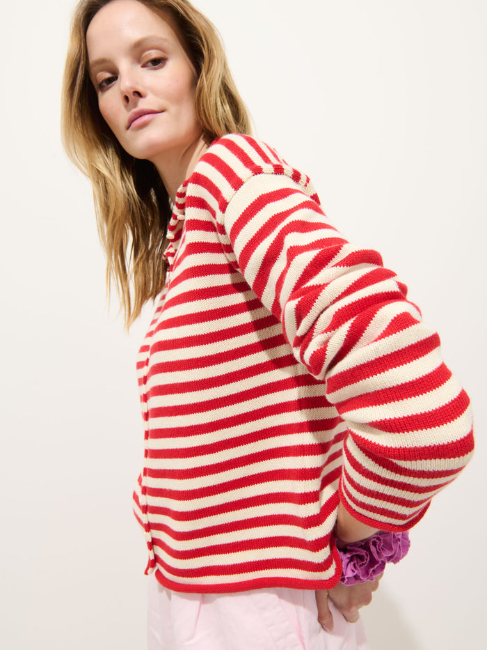 A blonde woman stands sideways in a Taylor Striped Cardigan in Cotton Cashmere—red and white stripes, oversized boxy fit—and light pink pants, with her hand on her hip against a plain white background.