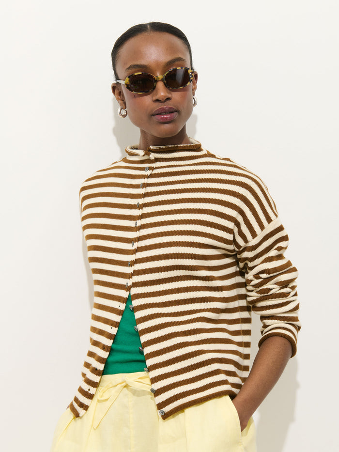 A person wearing the Taylor Striped Cardigan in Cotton Cashmere over a green top, yellow pants, hoop earrings, and tortoiseshell sunglasses stands against a plain light background.