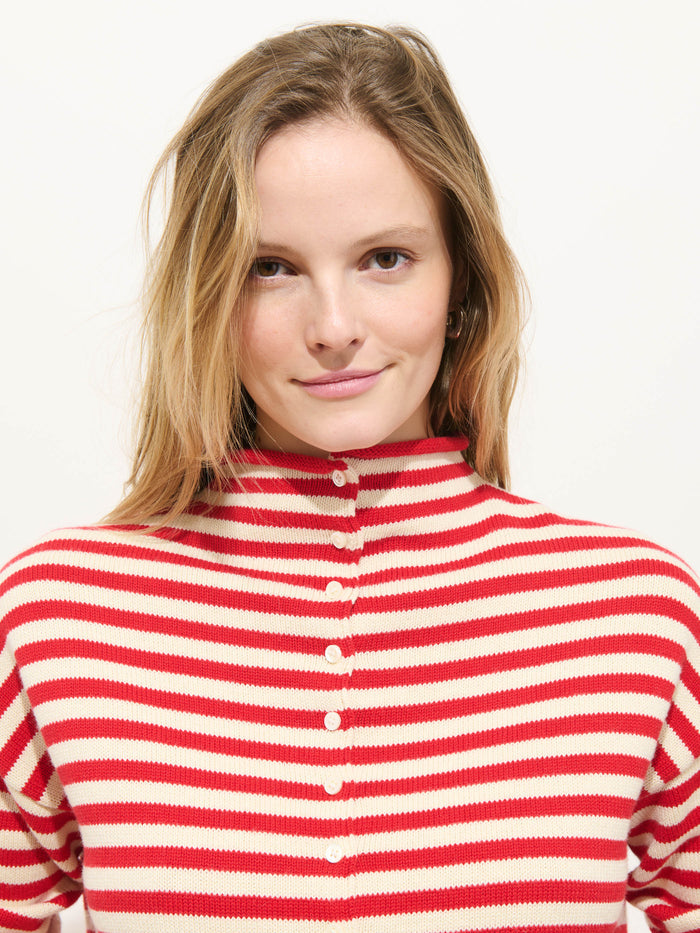 A person with long, light brown hair wears the Taylor Striped Cardigan in Cotton Cashmere with red and white stripes and Troca shell buttons, smiling gently at the camera against a plain white background.