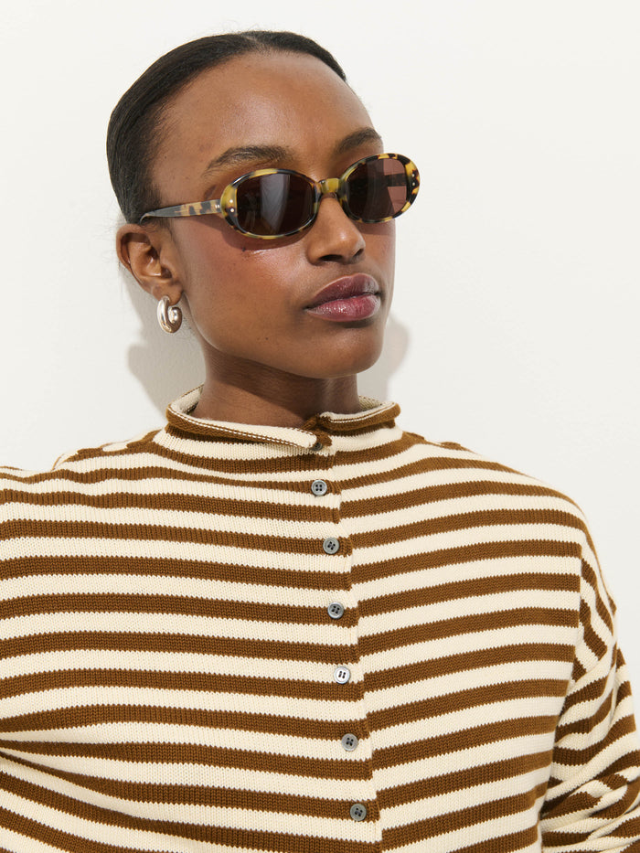 Wearing tortoiseshell sunglasses, silver hoop earrings, and the Taylor Striped Cardigan in Cotton Cashmere with an oversized boxy fit, a person stands against a plain white background.