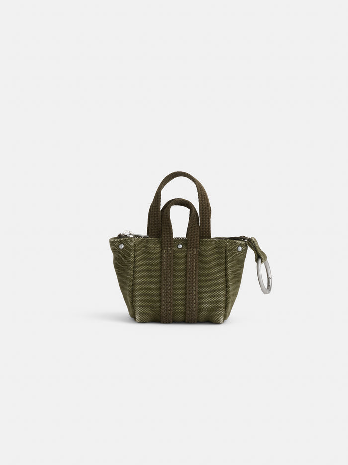 The Teeny Tiny Tote Keychain is a small olive green canvas miniature tote bag with two handles, visible stitching, and a zipper closure, featuring a functional keychain, shown against a plain white background.