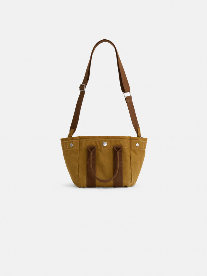 The Perfect Little Tote, a small brown canvas mini bag with dual top handles and an adjustable shoulder strap, is displayed on a plain white background.