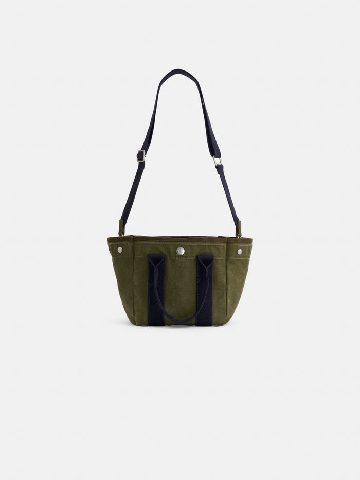 The Mini is a small olive green cotton canvas tote bag with dark blue handles and an adjustable shoulder strap, shown on a plain white background. Ideal for carrying your daily essentials.
