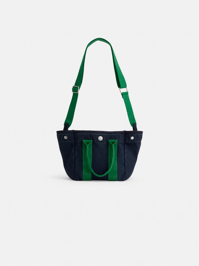 The Mini: a small navy blue cotton canvas tote bag with green handles and an adjustable green shoulder strap, shown on a plain white background.