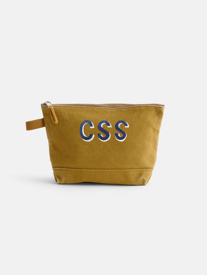 The Perfect Canvas Pouch in mustard yellow features "CSS" embroidered in blue and white on the front, a small side handle, and is shown against a plain white background.
