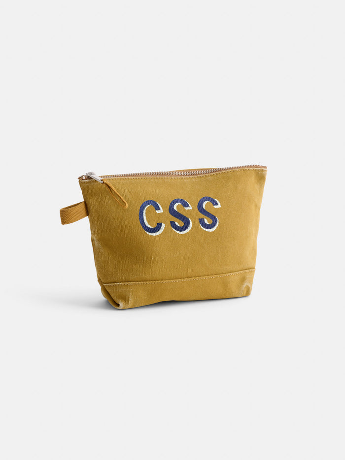 The Perfect Canvas Pouch is a mustard yellow pouch with a small loop handle, featuring bold white CSS letters outlined in blue on the front. It’s photographed against a plain white background.