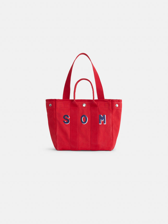 The Perfect Daily Tote is a red canvas cotton bag with two handles, featuring blue and white “SOM” lettering on the front. Set against a plain white background, this personalized tote is both stylish and functional.