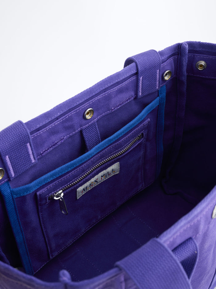 Open view of The Perfect Daily Tote in purple cotton, featuring an interior zippered pocket with a metallic Alex Mill label and blue trim, against a white background.
