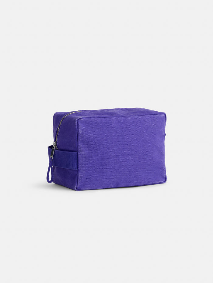 Introducing The Perfect Dopp Kit—a rectangular, purple fabric zippered pouch displayed against a white background. This minimalist canvas pouch features a small side handle and is ideal for use as a makeup bag or as a personalized toiletry bag.
