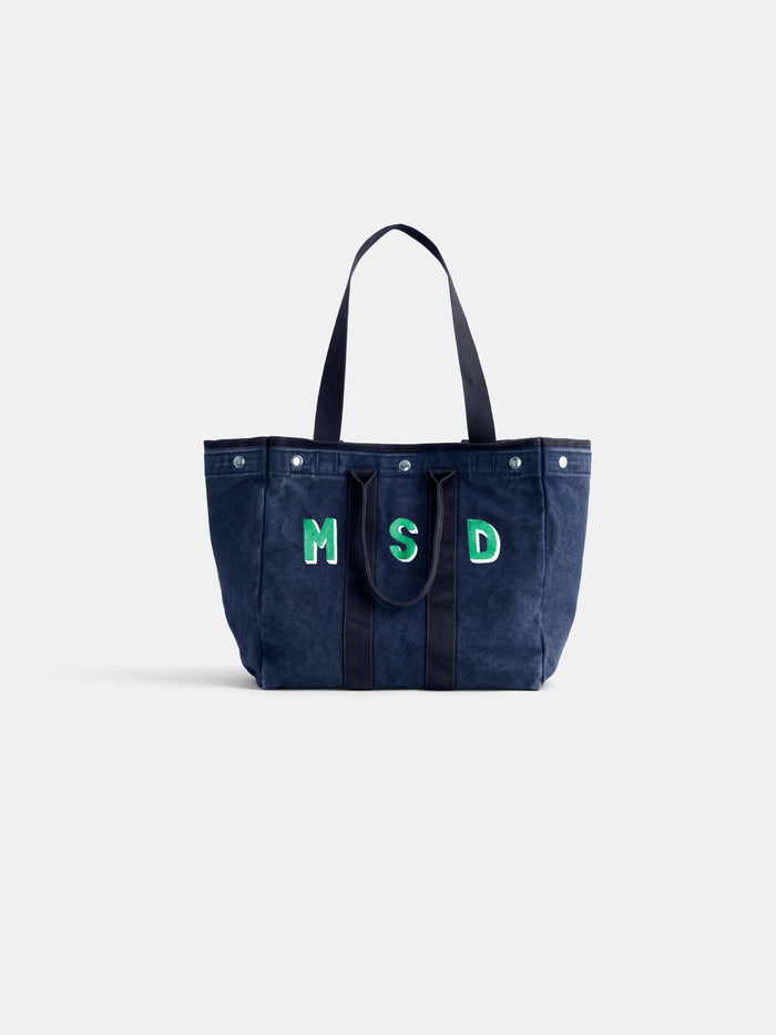 The Perfect Weekday Tote is a navy blue cotton bag with two handles, "MSD" in green and white on the front, and silver snap buttons for secure closure. Monogrammable for a personalized touch.
