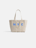 Introducing The Perfect Weekday Tote: crafted from beige cotton with sturdy double handles, this chic accessory showcases bold NYC lettering in blue across the front and is finished with silver rivets at the top corners. Ideal for daily use, it’s also part of our monogrammable tote bag collection—so you can personalize it to make it truly one-of-a-kind.