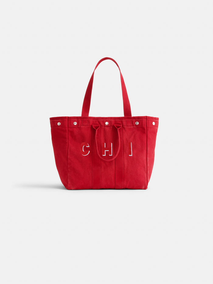 The Perfect Weekday Tote: a large red personalized bag with two handles, silver studs on the top edge, and "CHI" stitched in white on the front. Background is plain white.