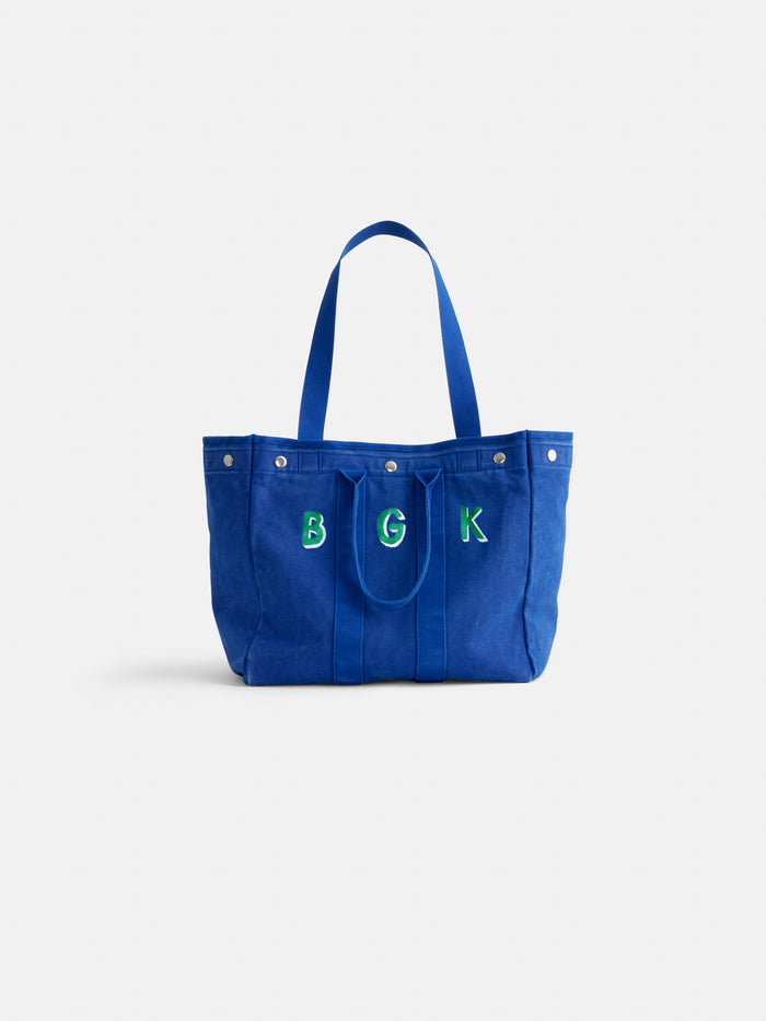 Introducing The Perfect Weekday Tote: a blue cotton bag with two sturdy handles, front snap buttons, and the letters B G K elegantly embroidered in green and white on the front—ideal for anyone who loves personalized accessories or is searching for a monogrammable tote bag.
