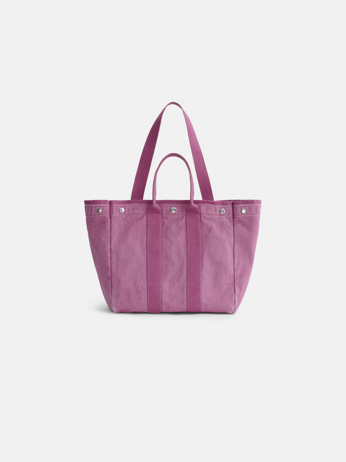 A pink cotton tote bag called The Perfect Weekday Tote, featuring two short handles, a long shoulder strap, and silver rivet accents, is displayed against a plain white background. This versatile bag combines classic style with functionality.