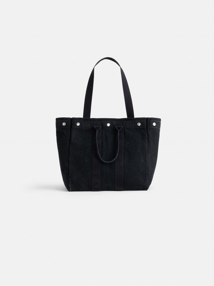The Perfect Weekday Tote by Alex Mill, crafted in black suede, features two long shoulder straps, two short handles, and silver snap button accents. Shown against a plain white background.