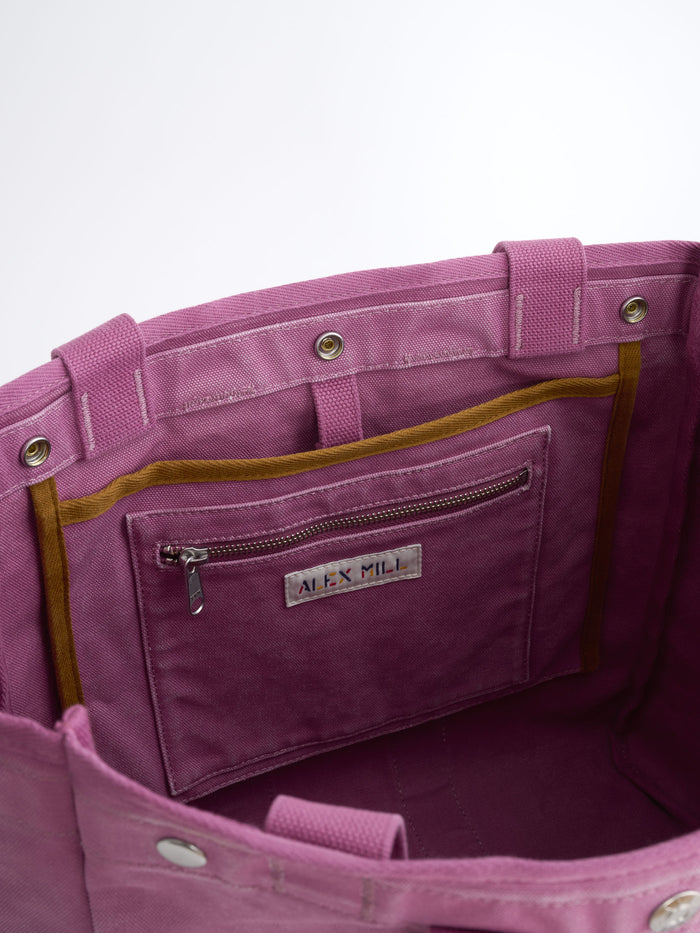 Close-up of the inside of The Perfect Weekday Tote in purple, featuring a zippered pocket, an ALEX MILL label, and brown trim details. Crafted from cotton with metal snaps and reinforced stitching, this spacious tote is designed to hold all your daily essentials. Ideal for those seeking a stylish and functional monogrammable bag.