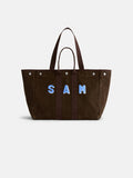 Sure! Here’s your rewritten sentence using the provided product data: A brown suede Painted Perfect Weekend Tote with dark handles and the name SAM in large blue and white letters on the front, displayed on a plain white background—this Alex Mill tote is perfect for those seeking stylish, monogrammable bags that make a personal statement.
