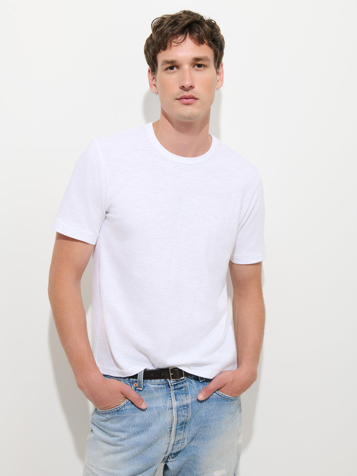 A young man stands against a plain white background with his hands in his pockets, looking directly at the camera while wearing The Standard T-Shirt In Slub Cotton.