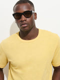 A man wearing black sunglasses and The Standard T-Shirt In Slub Cotton in yellow stands against a plain white background, looking directly at the camera with a neutral expression.