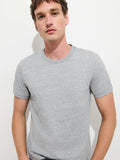 A person with short brown hair stands against a plain white background, wearing the Standard T-Shirt In Slub Cotton in light grey. The breathable fabric of the tee complements their neutral expression as they look at the camera.