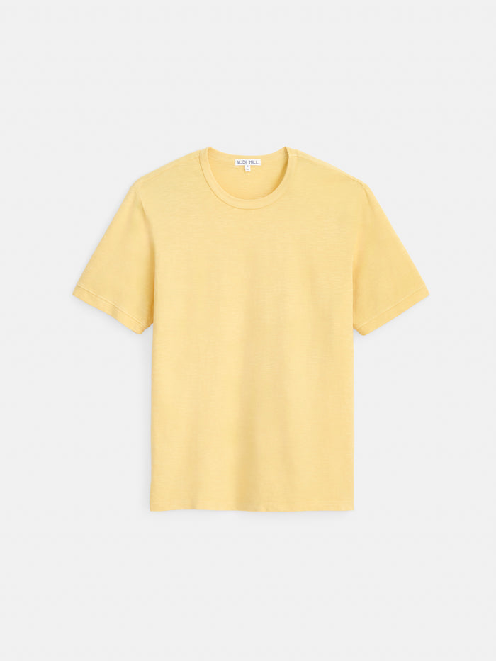 The Standard T-Shirt In Slub Cotton, a plain, short-sleeved men’s tee in light yellow, is laid flat against a white background and crafted from breathable slub cotton for all-day comfort.