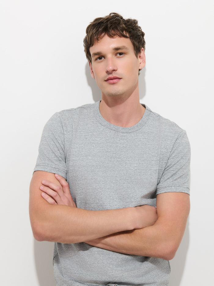 A young man with short brown hair, wearing the Standard T-Shirt In Slub Cotton in light gray, stands against a plain white background with his arms crossed, looking at the camera with a neutral expression.