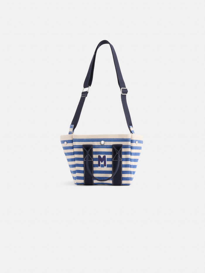The Striped Mini is a cotton canvas tote with blue and white stripes, navy handles, an adjustable strap, and a bold M logo on the front. This monogrammable bag is shown against a plain white background.
