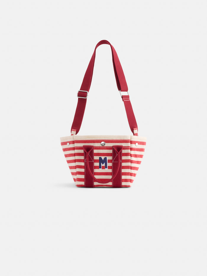 The Striped Mini is a small tote with red and white stripes, red handles, an adjustable red shoulder strap, and a blue "M" monogram on the front pocket.
