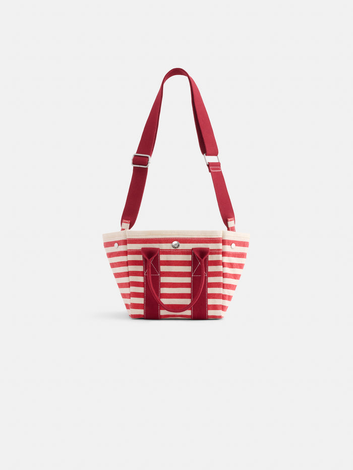 The Striped Mini is a stylish mini tote bag with red and white horizontal stripes, red handles, an adjustable shoulder strap, and a front snap pocket—perfect for monogramming on a plain white background.