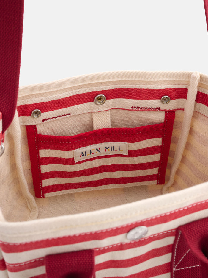 Interior view of The Striped Mini, a red and white striped tote bag with a small pocket, ALEX MILL label, red handles, and metal snap closures—a stylish, monogrammable accessory.