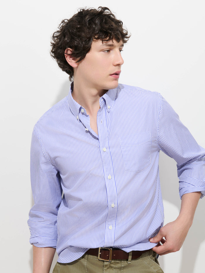 A person with curly brown hair wearing the Mill Striped Shirt in Thomas Mason and khaki pants looks to the side against a plain white background.