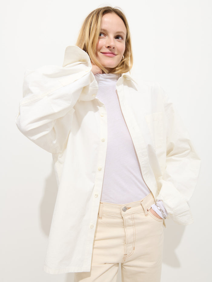 A person with blonde hair smiles softly while wearing a white oversized button-up shirt over the Tissue Turtleneck In Cotton and light beige pants, posing against a plain white background.