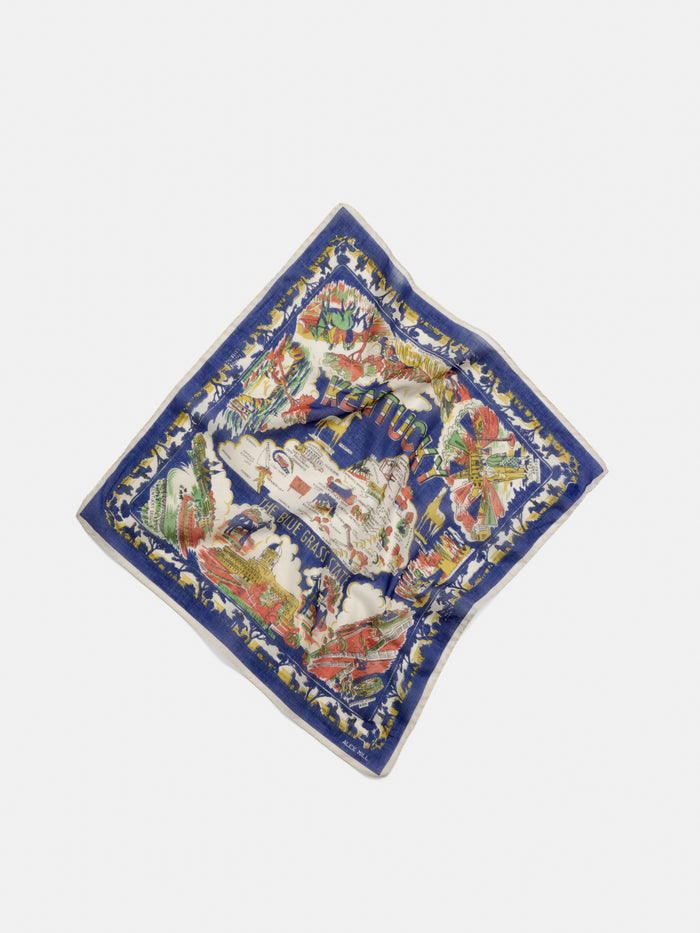 A vibrant Travel Scarf In Cotton Voile with a blue border, showcasing an illustrated map of Capri, Italy alongside iconic landmarks and floral motifs. Evoking the charm of a vintage bandana, the scarf is displayed flat against a white background.