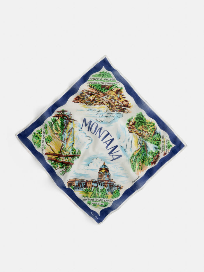 The Travel Scarf In Cotton Voile is a square accessory made from soft cotton voile, adorned with vibrant illustrations of iconic Montana landmarks—like mountains, a ship, and the Montana State Capitol. Inspired by vintage bandana styles, it features “Montana” boldly displayed at the center for a timeless look.