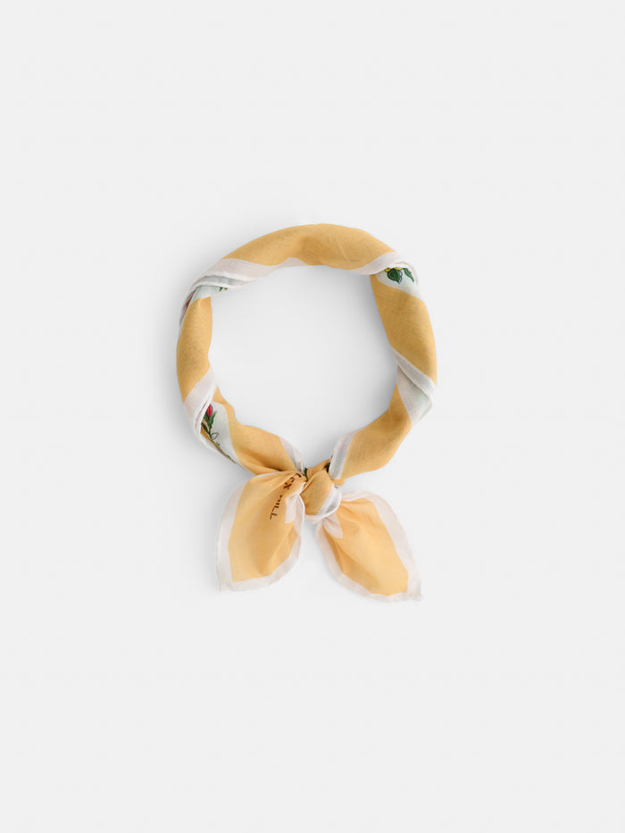 The Travel Scarf In Cotton Voile, shown in yellow and white with a subtle pattern, is tied in a simple knot and arranged in a circle on a plain white background.