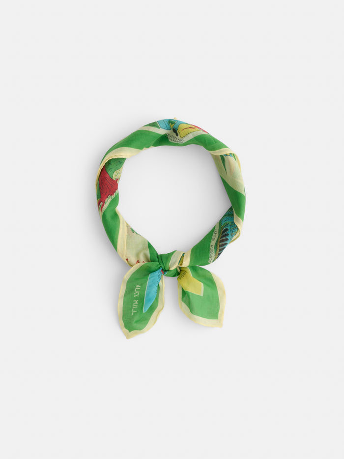 The Travel Scarf in Cotton Voile, featuring a green, yellow, and red vintage bandana pattern, is tied in a simple knot against a plain white background.