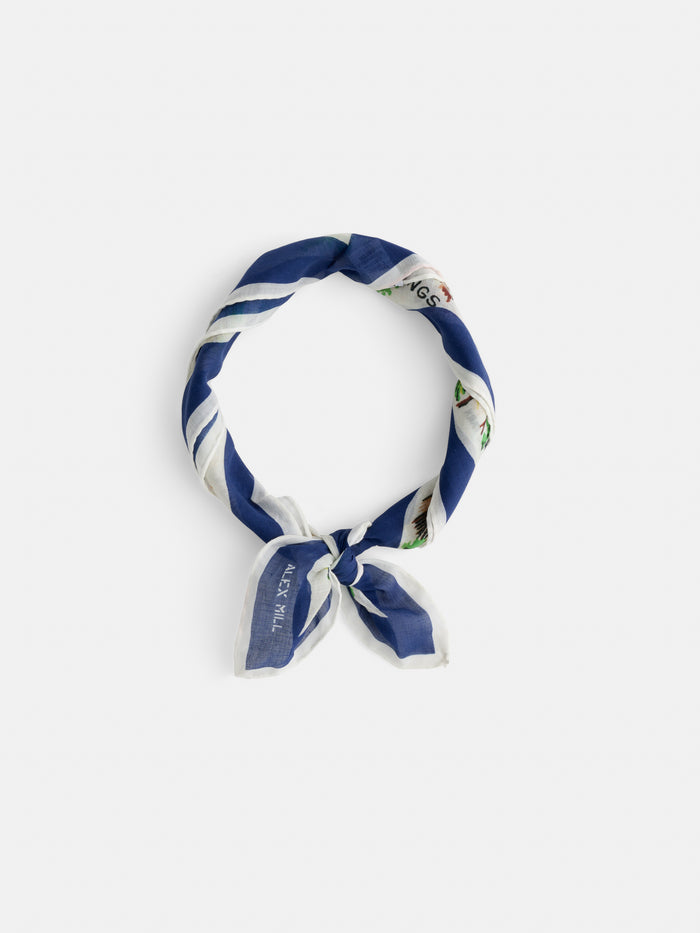 Travel Scarf In Cotton Voile, featuring blue and white stripes, crafted from soft cotton voile, styled in a loop with a knot at the bottom and presented against a plain white background.
