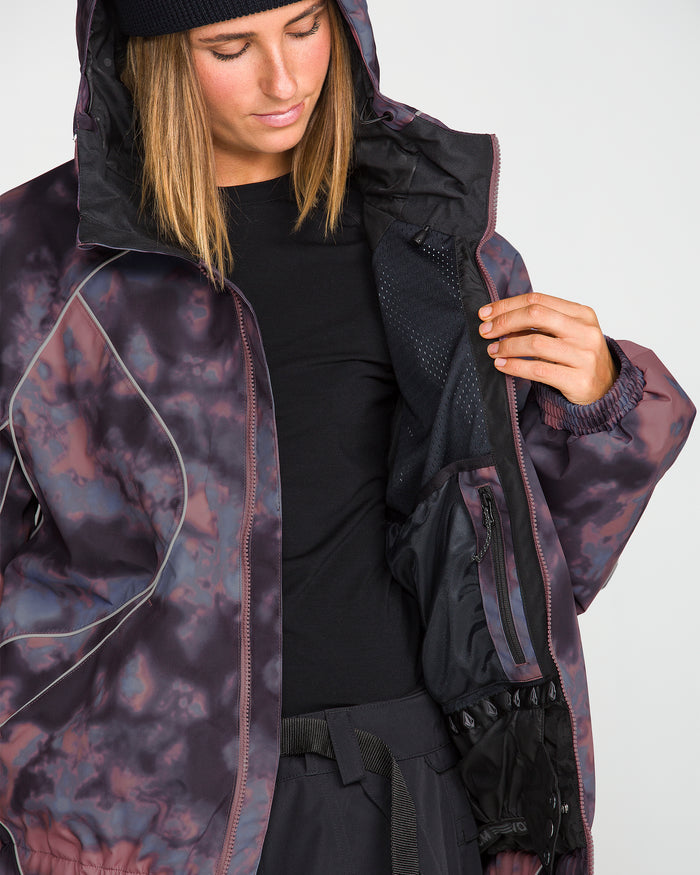 A person wearing the Volcom Unisex Liftline 20K Jacket—a baggy fit snowboard jacket with a hooded, patterned design—looks down and opens the jacket to reveal its mesh inner pocket, 20K waterproof lining, and zippered compartments.