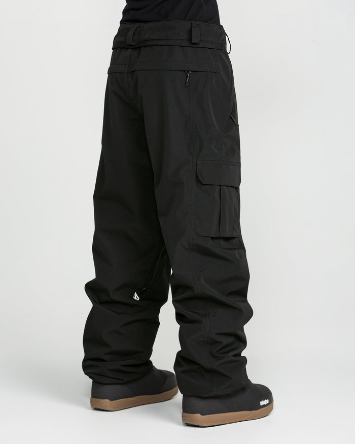 A person wearing Volcom’s Unisex Liftline 20K Pants in black recycled fabric and black winter boots with brown soles stands against a plain white background. The image is focused on the pants from the waist down.
