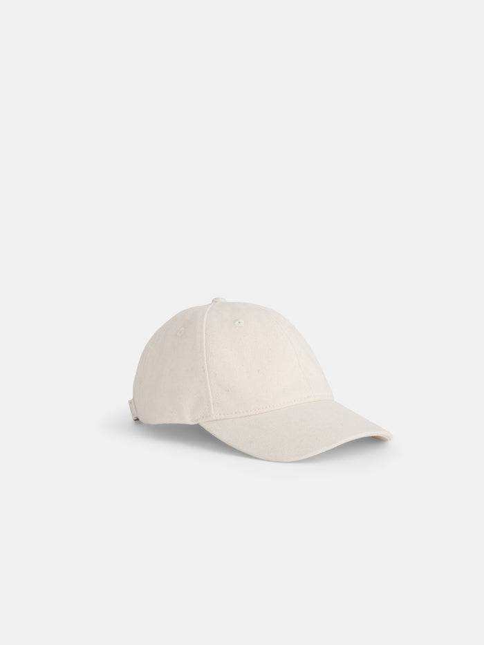The Washed Canvas Baseball Cap in light beige features a curved brim, stitched eyelets, and an adjustable back strap, shown against a white background.