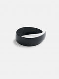 The Wide Headband, handcrafted from premium acetate, features a sleek, glossy black crescent shape and minimalist design with a slightly curved, wide structure. It is displayed on a plain white background.