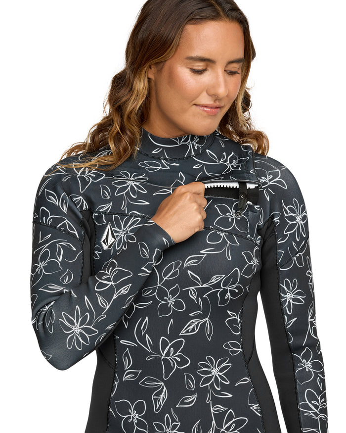 A woman wearing the Volcom Women's 2/2 Modulator Long Sleeve Spring wetsuit unzips a small front pocket, smiling and looking down.