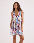 A woman models the Volcom Women's A-Line Swing Dress, a sleeveless, V-neck woven day dress featuring pink, blue, and green floral prints. She stands against a plain light background with her hands in the dress pockets.