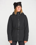 A woman wearing the Volcom Women’s Alpine All Day Insulated Jacket with a belt and a black beanie stands facing forward against a plain white background, smiling slightly.