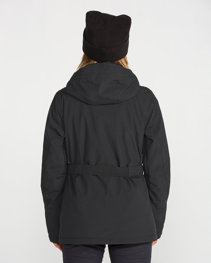 A person wearing the Volcom Women’s Alpine All Day Insulated Jacket in black, featuring a hood, along with a black hat, is seen from behind standing against a plain white background.